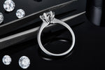 CARISSIE round moissanite solitaire ring, resting on tweezers to reveal the detailed craftsmanship of the sculpted prongs