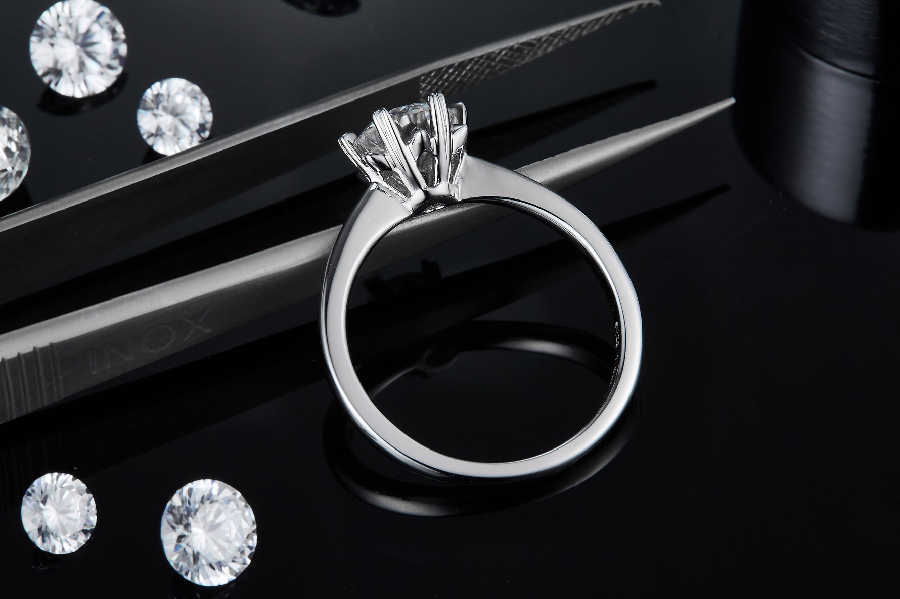 CARISSIE round moissanite solitaire ring, resting on tweezers to reveal the detailed craftsmanship of the sculpted prongs