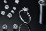CARISSIE round moissanite solitaire ring, artistic shot on a dark background with scattered loose stones and reflection