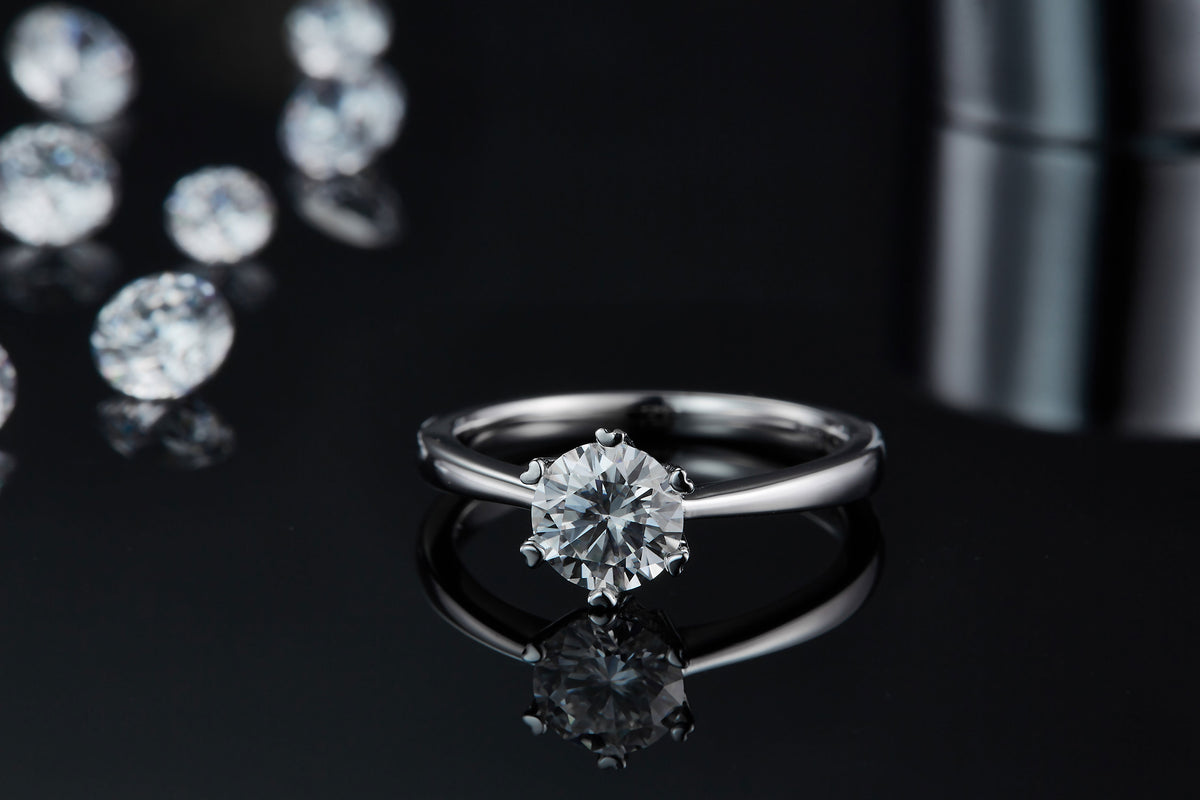 CARISSIE round moissanite solitaire ring, front view on black surface displaying the gemstone sparkle and mirror-like reflection