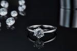 CARISSIE round moissanite solitaire ring, front view on black surface displaying the gemstone sparkle and mirror-like reflection