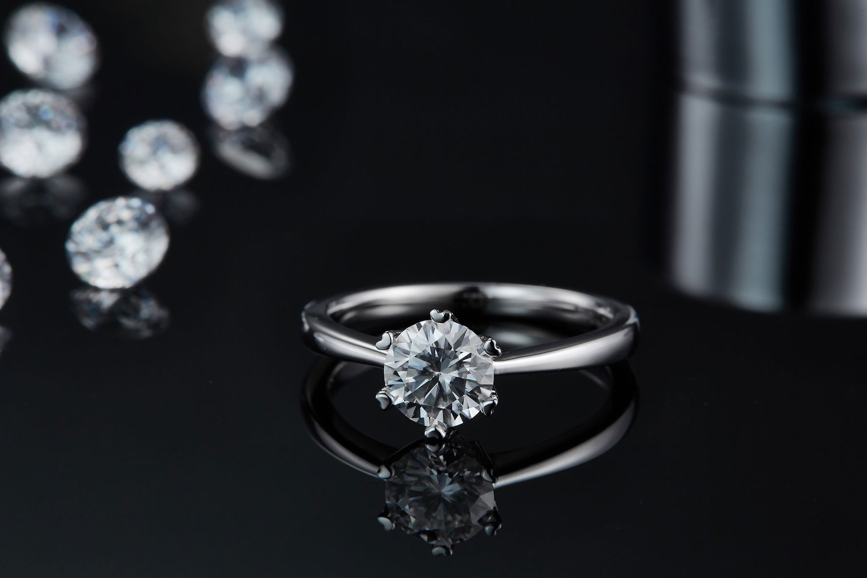 CARISSIE round moissanite solitaire ring, front view on black surface displaying the gemstone sparkle and mirror-like reflection