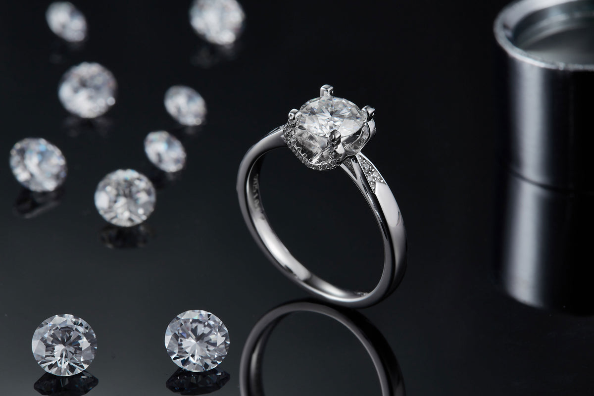 CARISSIE round moissanite solitaire ring, lifestyle shot on black background surrounded by loose stones and metal tool