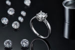 CARISSIE round moissanite solitaire ring, lifestyle shot on black background surrounded by loose stones and metal tool