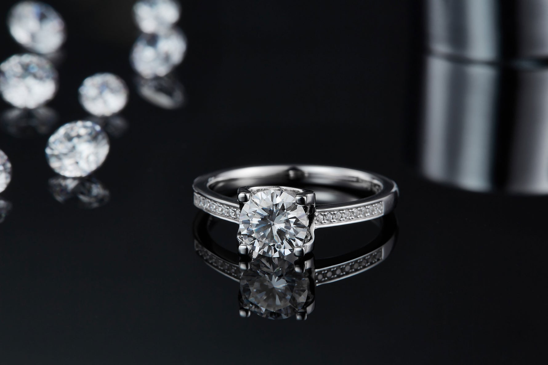 CARISSIE round moissanite solitaire ring, low-angle view on reflective black surface emphasizing side profile and sparkle