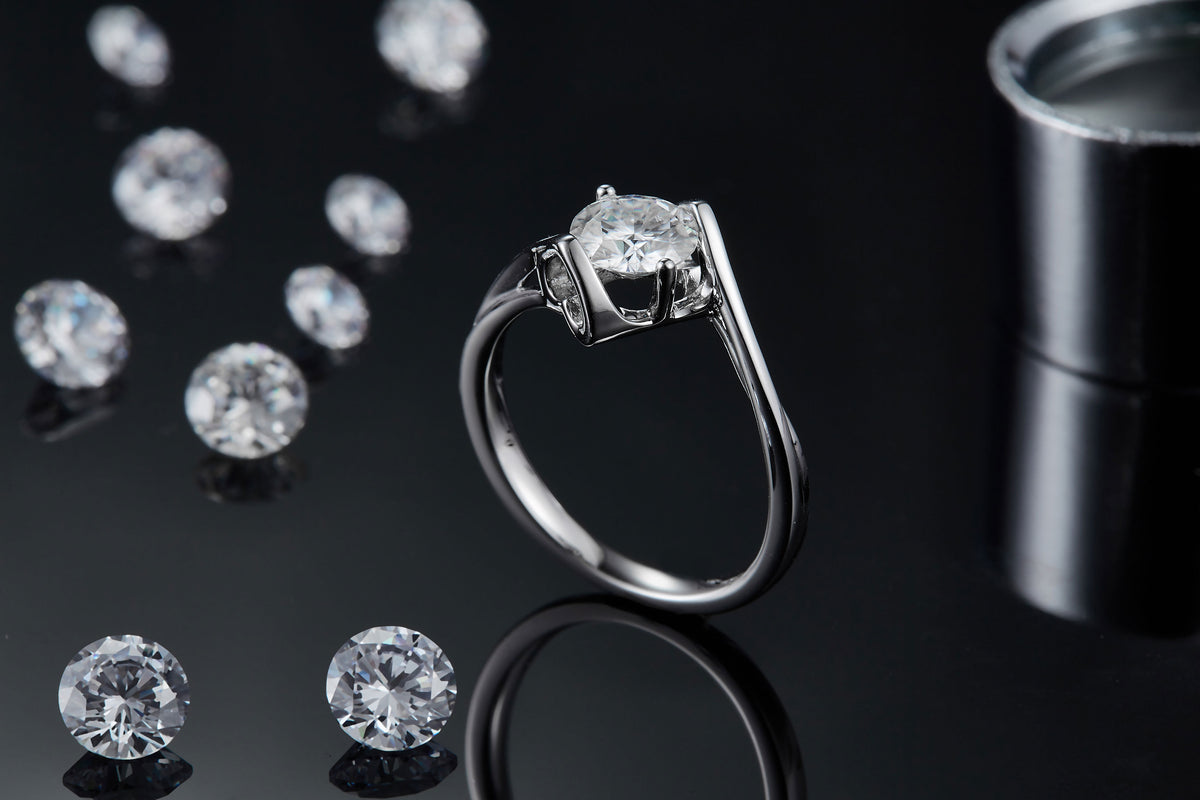 CARISSIE round moissanite tension ring, lifestyle shot on black background with loose stones and a cylindrical container