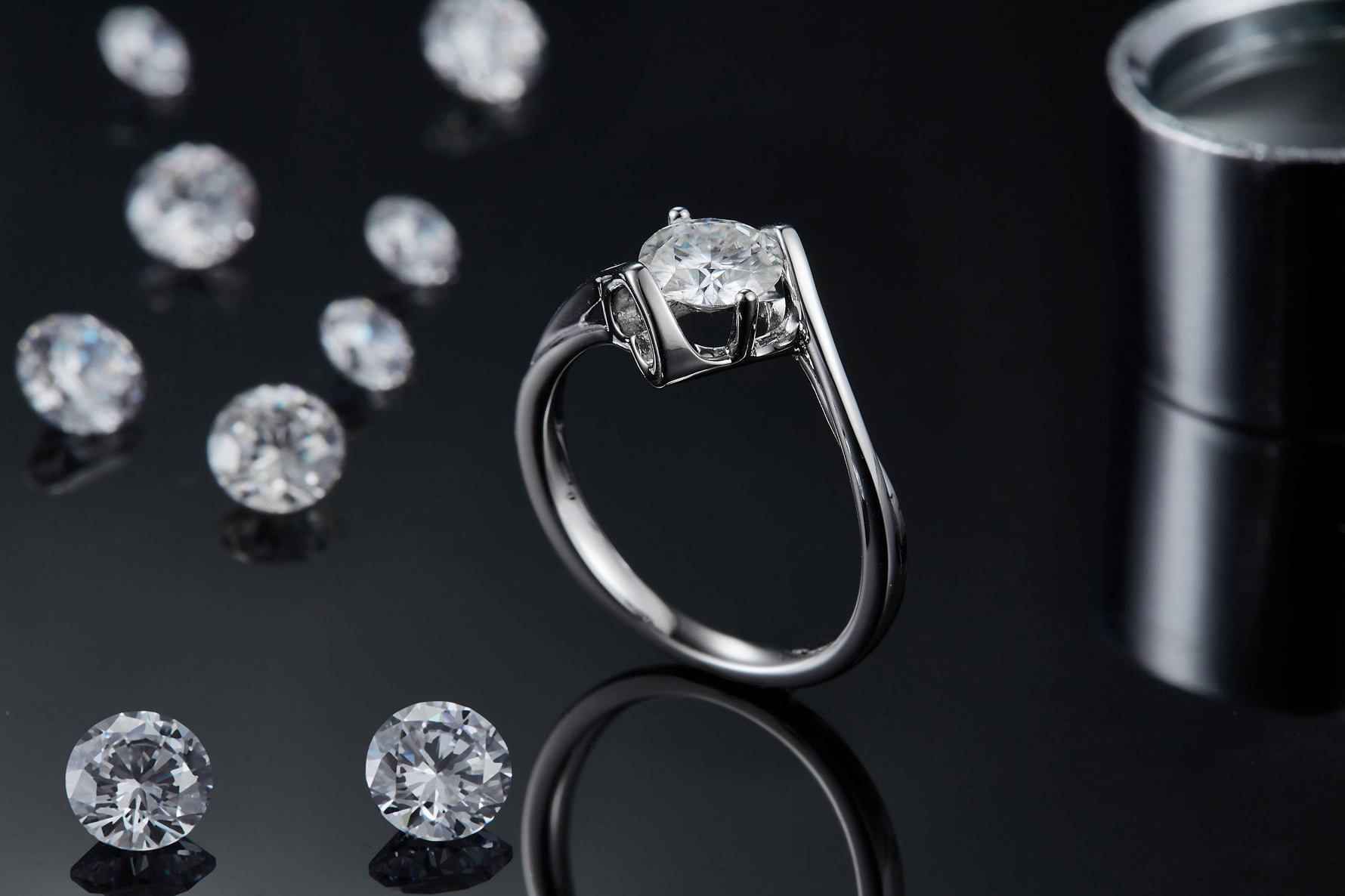 CARISSIE round moissanite tension ring, lifestyle shot on black background with loose stones and a cylindrical container