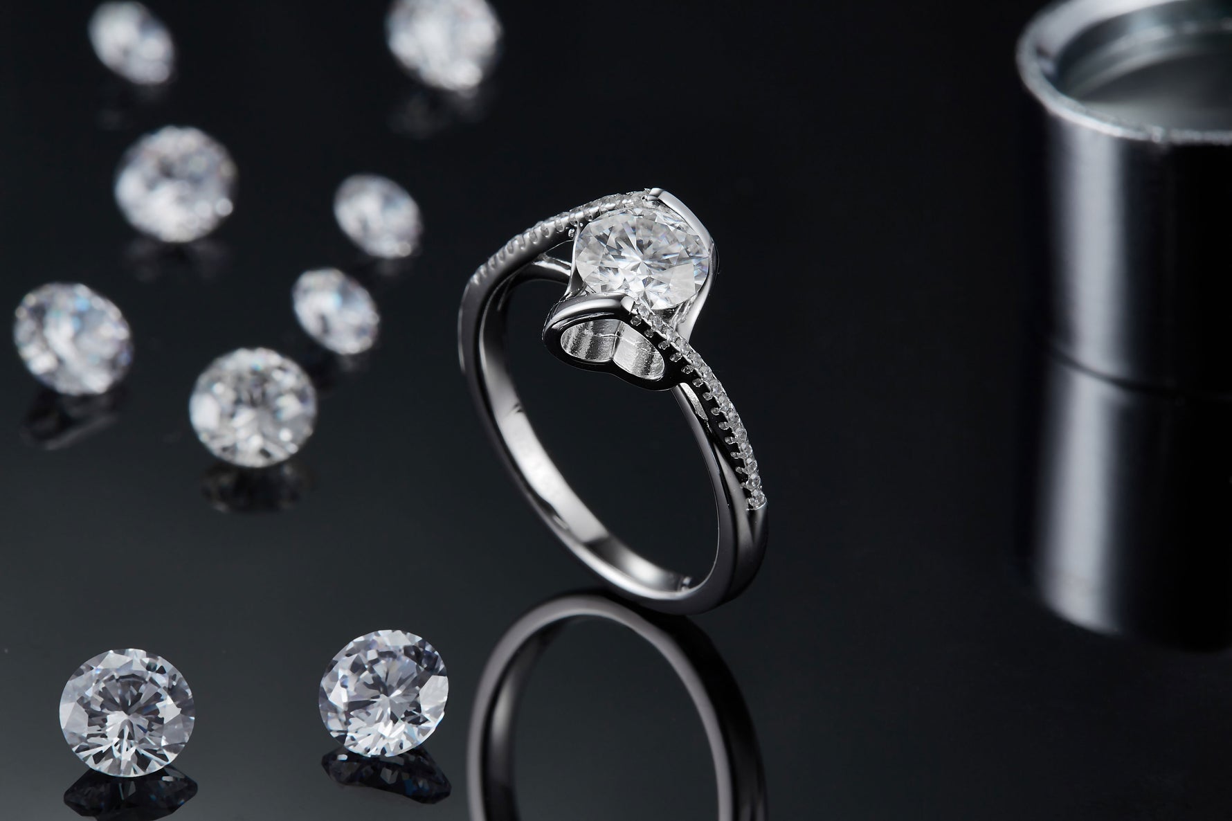 CARISSIE round moissanite bezel ring, artistic lifestyle shot on a dark surface with loose stones in the background.