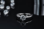 CARISSIE round moissanite solitaire ring, reflection shot on dark surface showcasing symmetry and brilliance of the gemstone