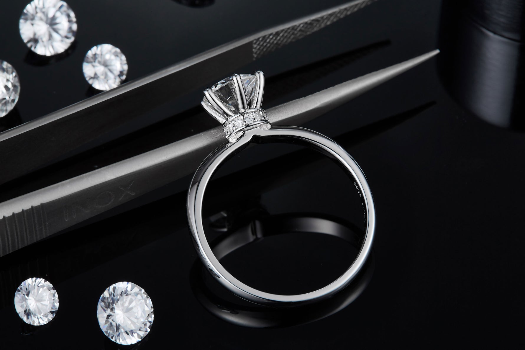 CARISSIE round moissanite solitaire ring, detail shot resting near tweezers to showcase craftsmanship and scale