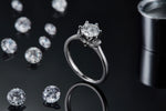 CARISSIE round moissanite solitaire ring, artistic lifestyle shot on black background with scattered loose gems