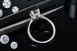 CARISSIE round moissanite solitaire ring, close-up detail of the H-shaped pavé setting held by tweezers next to loose gems