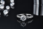 CARISSIE round moissanite solitaire ring, lifestyle shot on reflective surface emphasizing the sparkle of the main stone and side accents