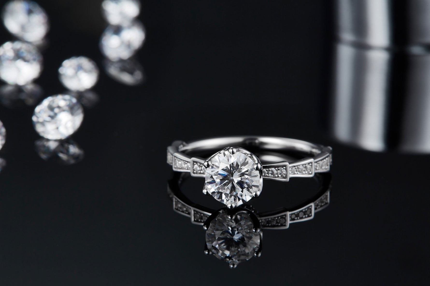 CARISSIE round moissanite solitaire ring, lifestyle shot on reflective surface emphasizing the sparkle of the main stone and side accents