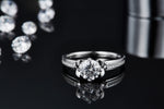 CARISSIE round moissanite solitaire ring, front lifestyle shot with reflection, emphasizing the sparkle of the center stone