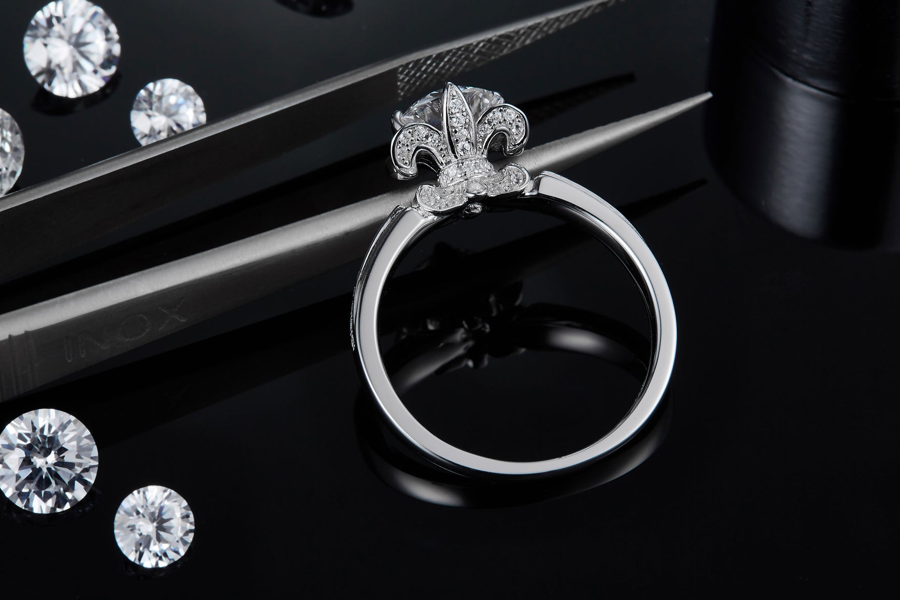 CARISSIE round moissanite solitaire ring, close-up view held by tweezers showcasing the intricate pavé details on the fleur-de-lis