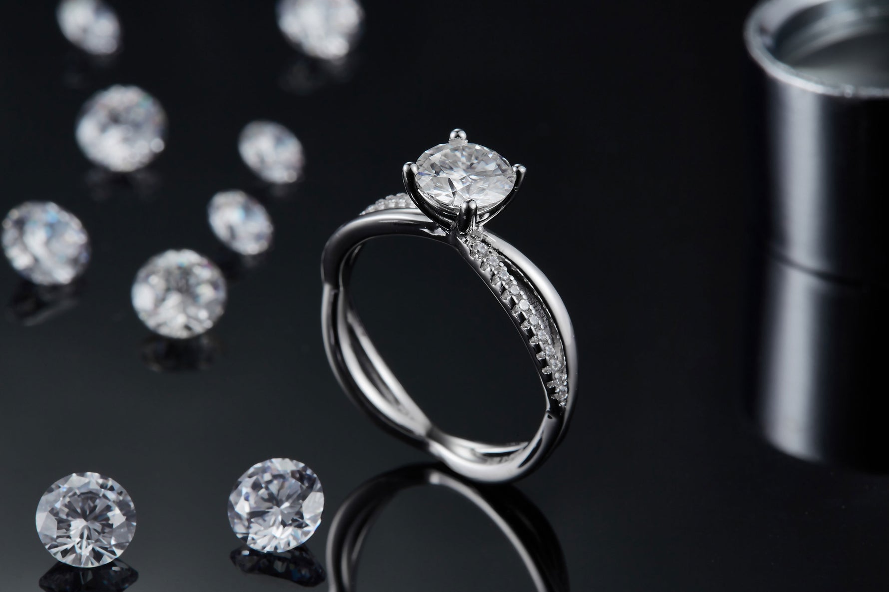 CARISSIE round moissanite solitaire ring, lifestyle shot on black background with loose stones, emphasizing the ring's sparkle and height