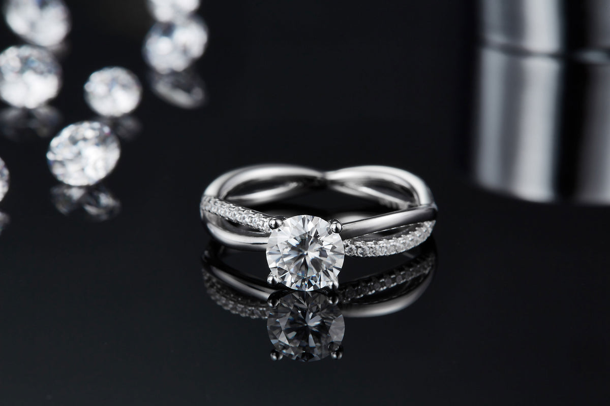 CARISSIE round moissanite solitaire ring, front angle on reflective surface showing clear reflection of the center stone and split band