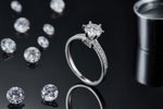 CARISSIE round moissanite solitaire ring, lifestyle shot on a dark reflective surface with loose gemstones in the background