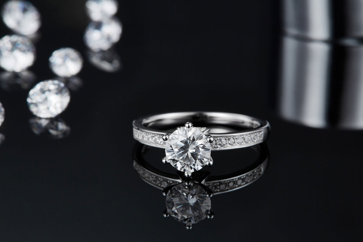 CARISSIE round moissanite solitaire ring, close-up on black mirror displaying the clear reflection of the silver-tone setting