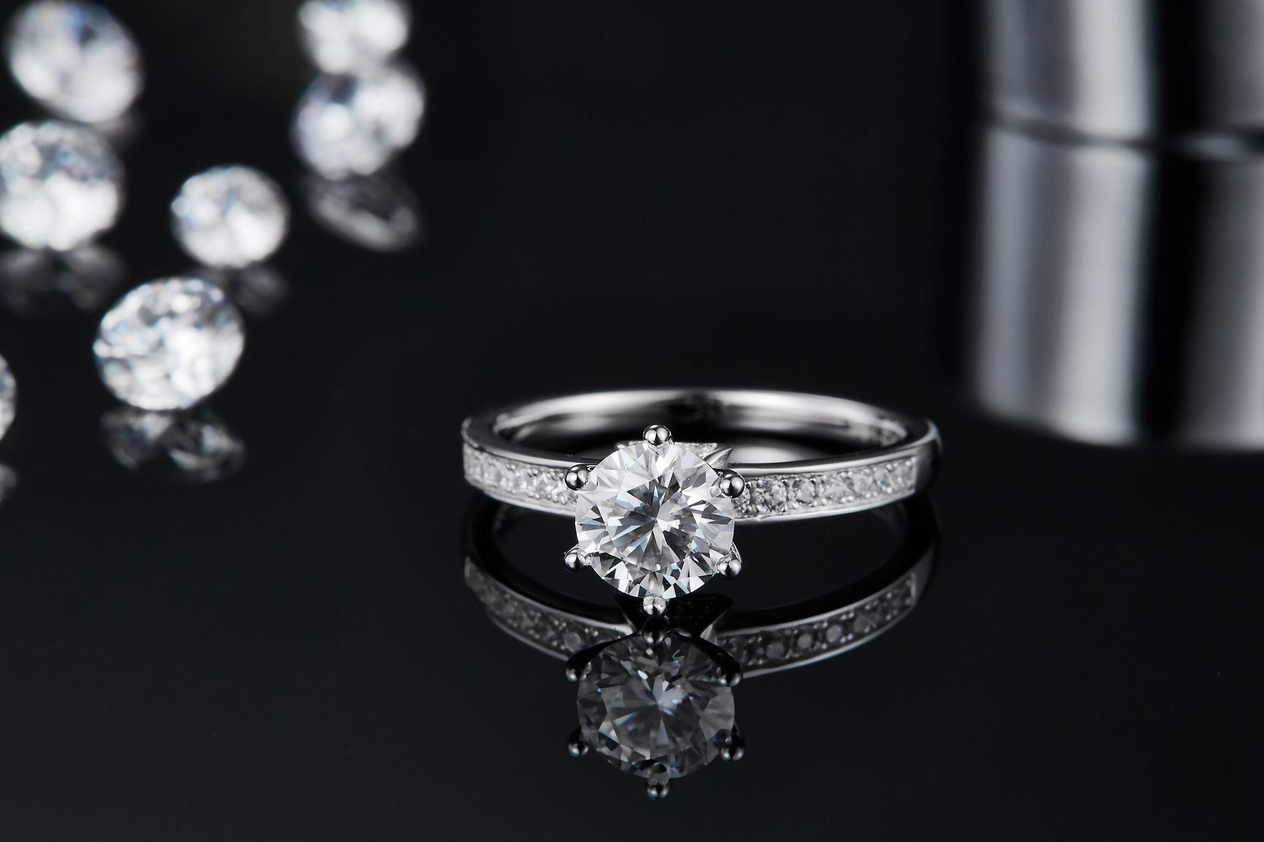 CARISSIE round moissanite solitaire ring, close-up on black mirror displaying the clear reflection of the silver-tone setting