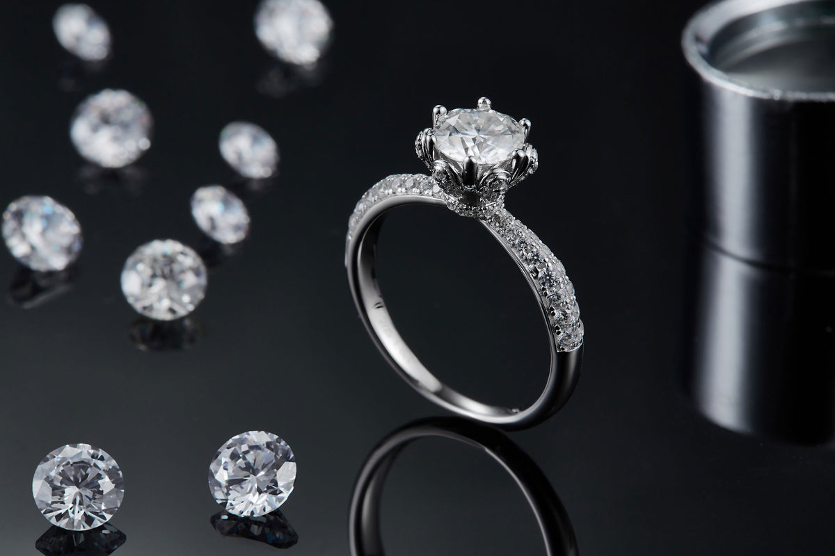 CARISSIE round moissanite solitaire ring, lifestyle shot on black background with loose stones and reflection