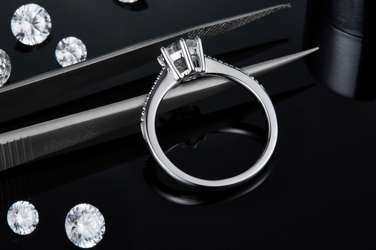 CARISSIE round moissanite solitaire ring, close-up held by tweezers revealing the interior structure of the prongs