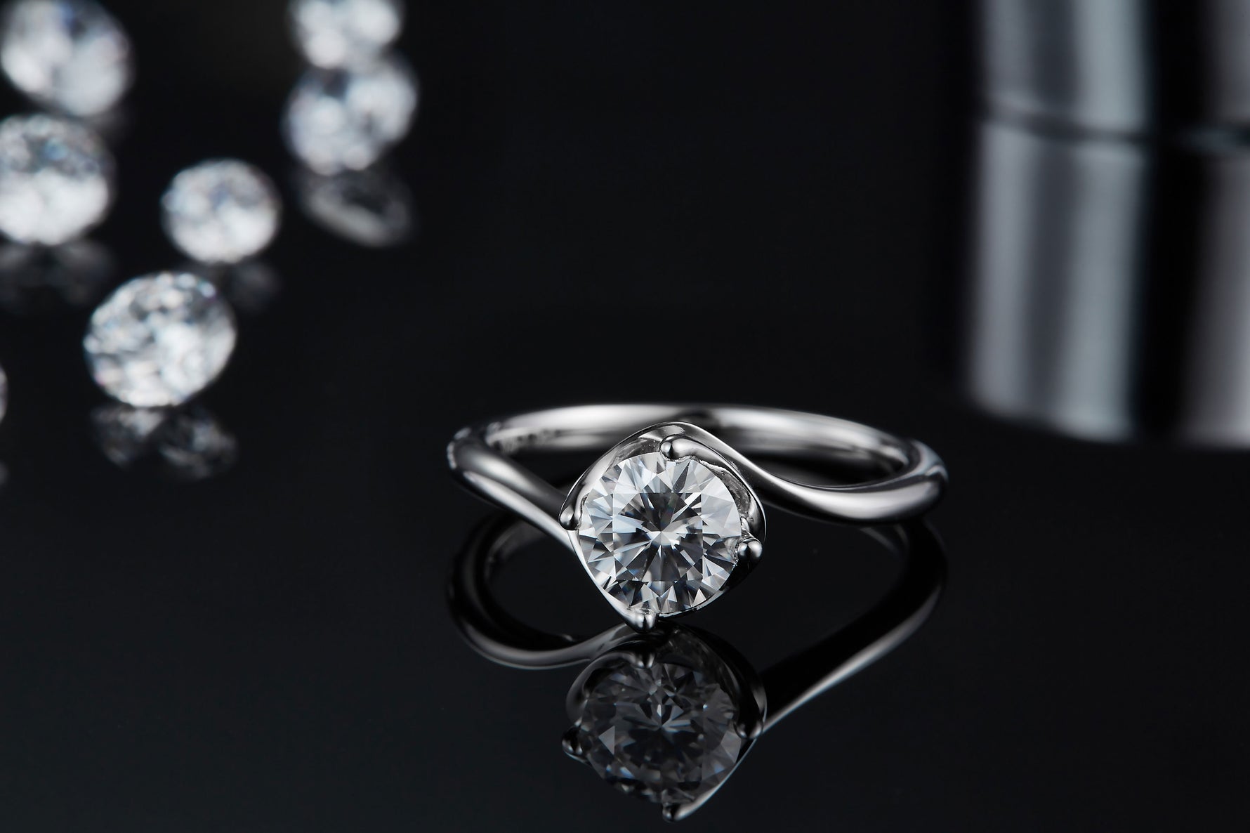 CARISSIE round moissanite solitaire ring, lifestyle shot resting on dark reflective surface with blurred gems in background