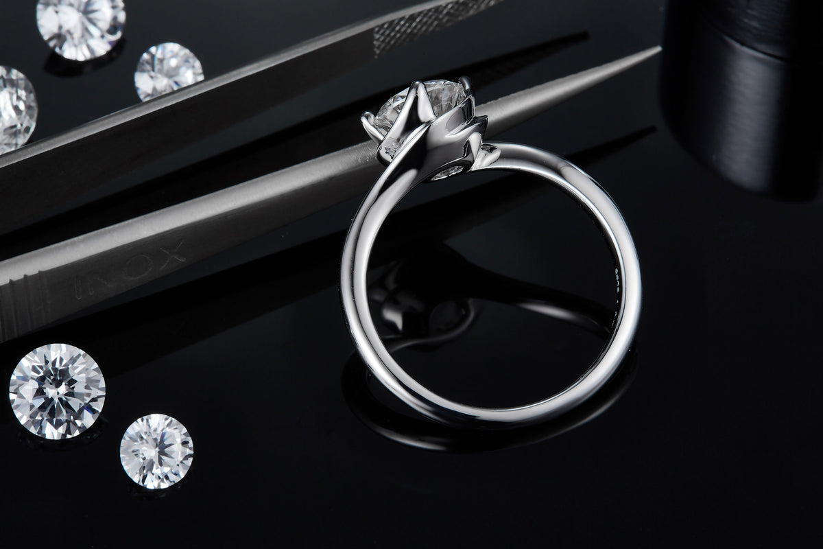 CARISSIE round moissanite solitaire ring, close-up side view held by tweezers showing detailed prongs and inner band markings