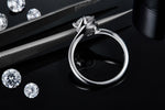 CARISSIE round moissanite solitaire ring, close-up side view held by tweezers showing detailed prongs and inner band markings