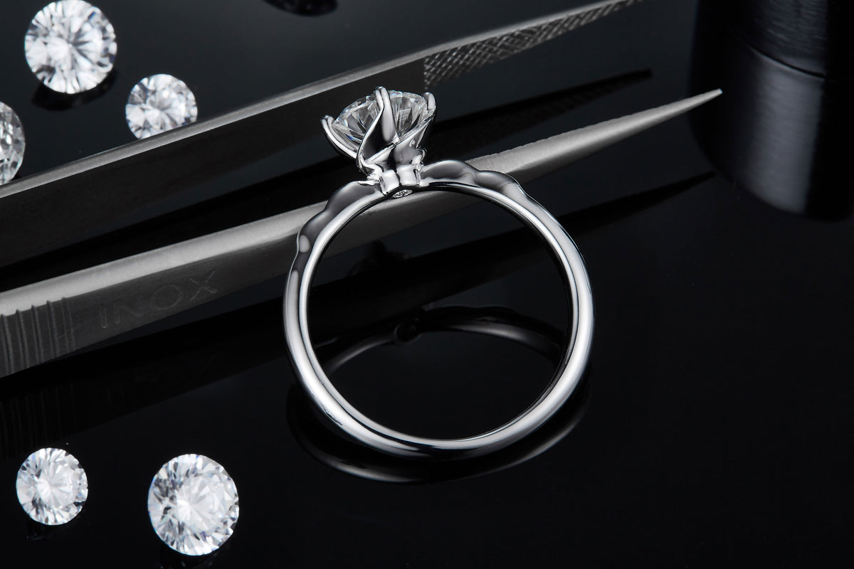 CARISSIE round moissanite solitaire ring, side angle held by tweezers to display the petal-inspired prongs holding the stone