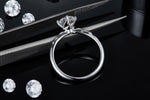 CARISSIE round moissanite solitaire ring, side angle held by tweezers to display the petal-inspired prongs holding the stone