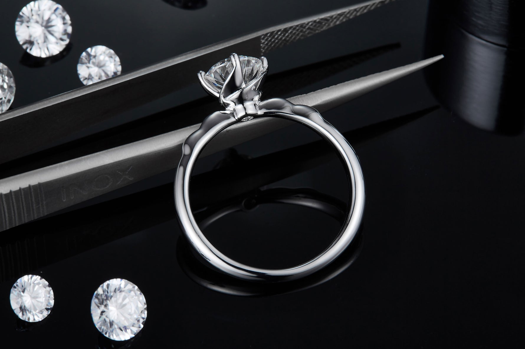 CARISSIE round moissanite solitaire ring, side angle held by tweezers to display the petal-inspired prongs holding the stone