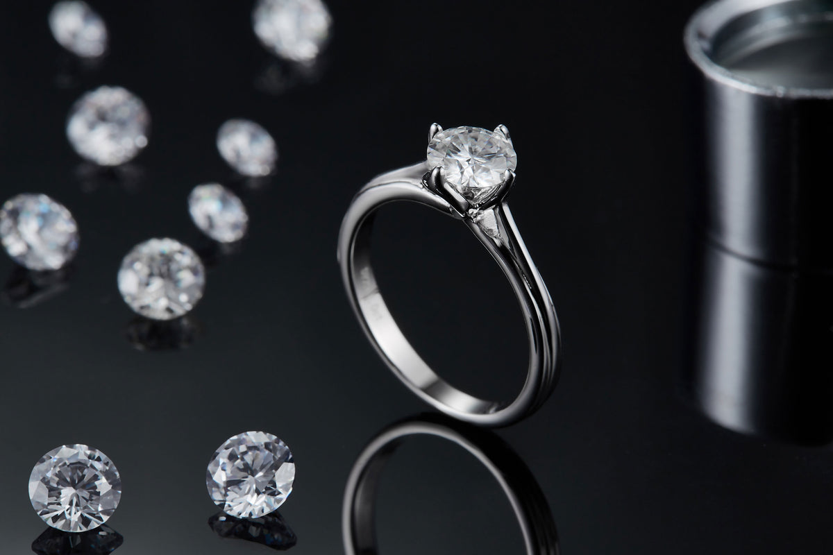CARISSIE round moissanite solitaire ring, lifestyle shot with loose stones showcasing sparkle and prong detail
