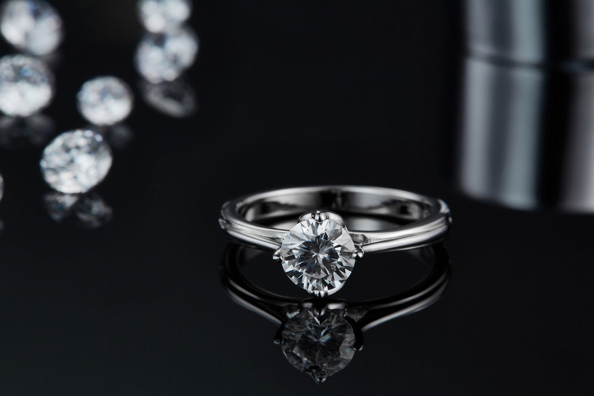 CARISSIE round moissanite solitaire ring, reflection on black surface emphasizing the modern split shank design