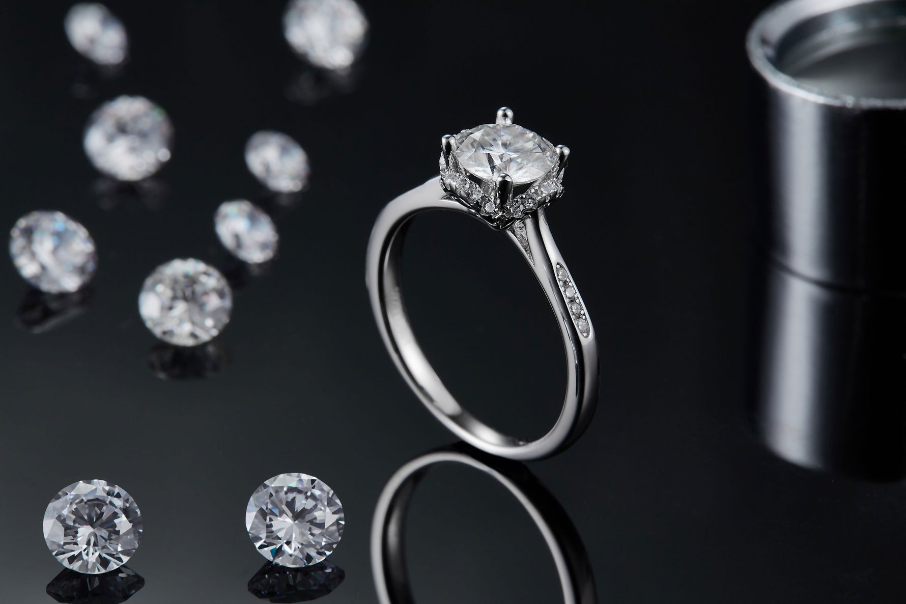 CARISSIE round moissanite halo engagement ring, lifestyle shot standing upright on black surface with loose stones in background