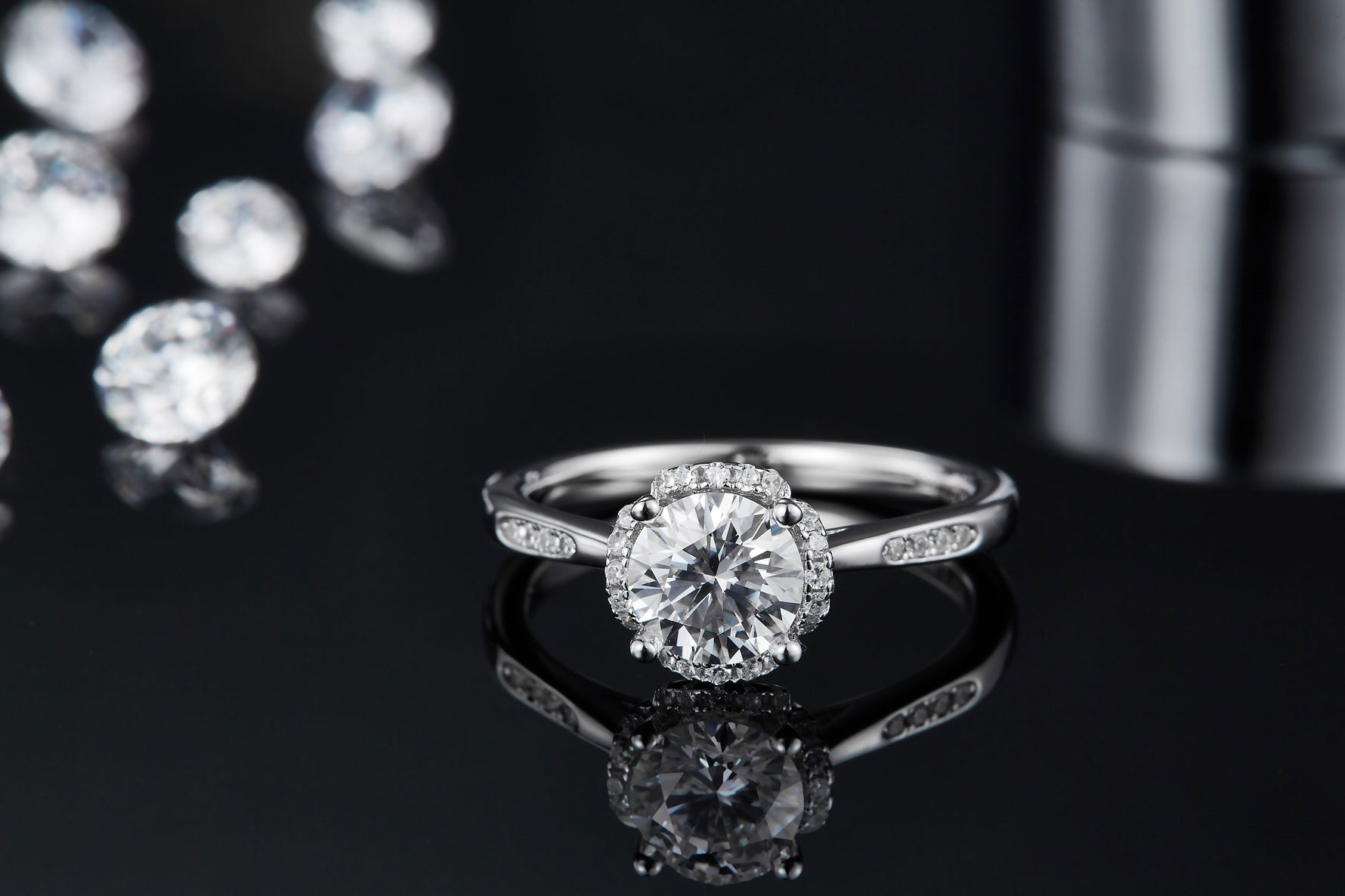 CARISSIE round moissanite halo engagement ring, front view resting on reflective black surface with clear mirror-like reflection
