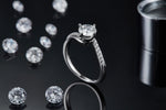 CARISSIE round moissanite solitaire ring, lifestyle shot standing on black surface surrounded by loose moissanite gems
