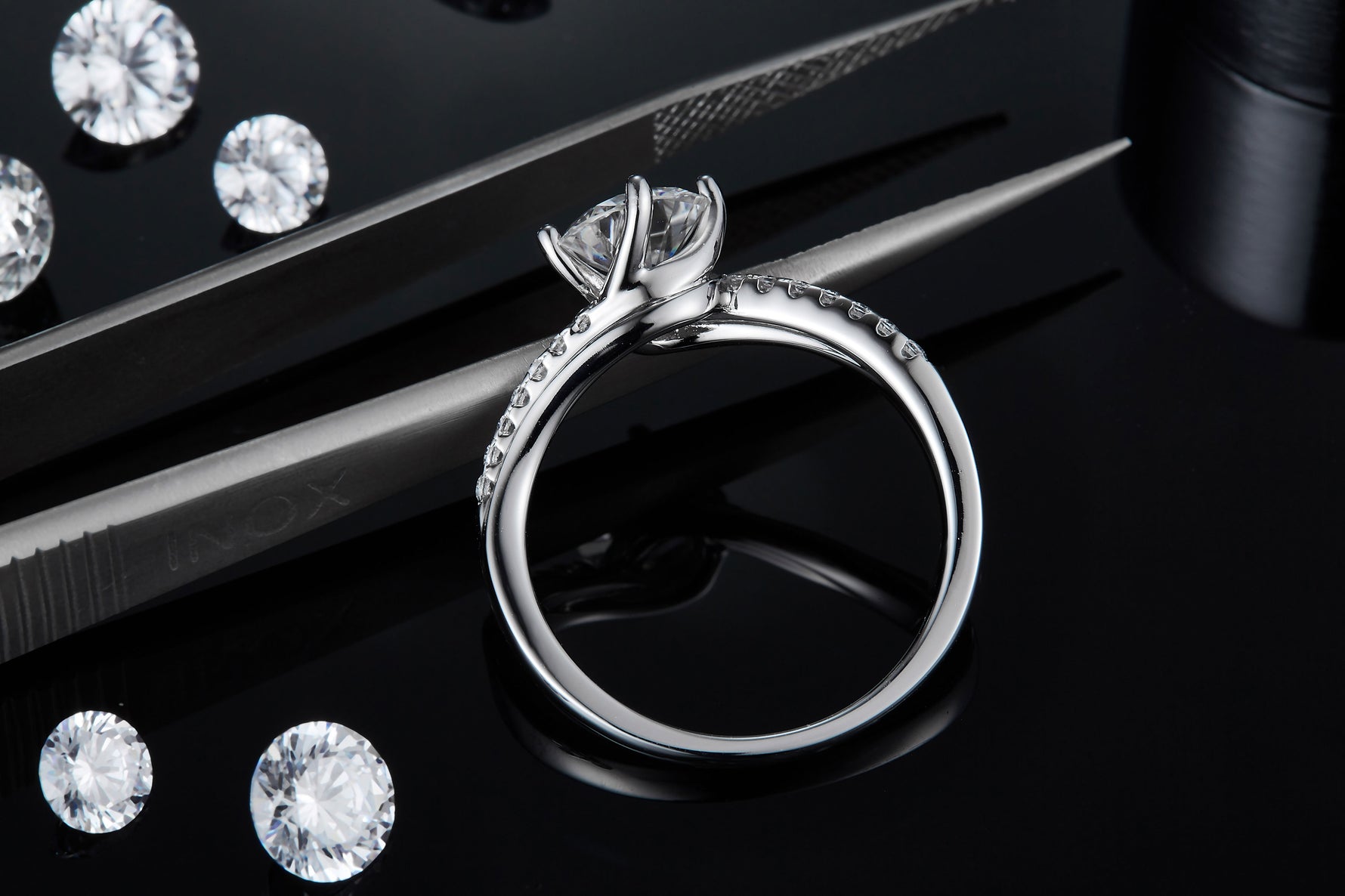 CARISSIE round moissanite solitaire ring, resting on tweezers to display the inner band structure and side-set stones