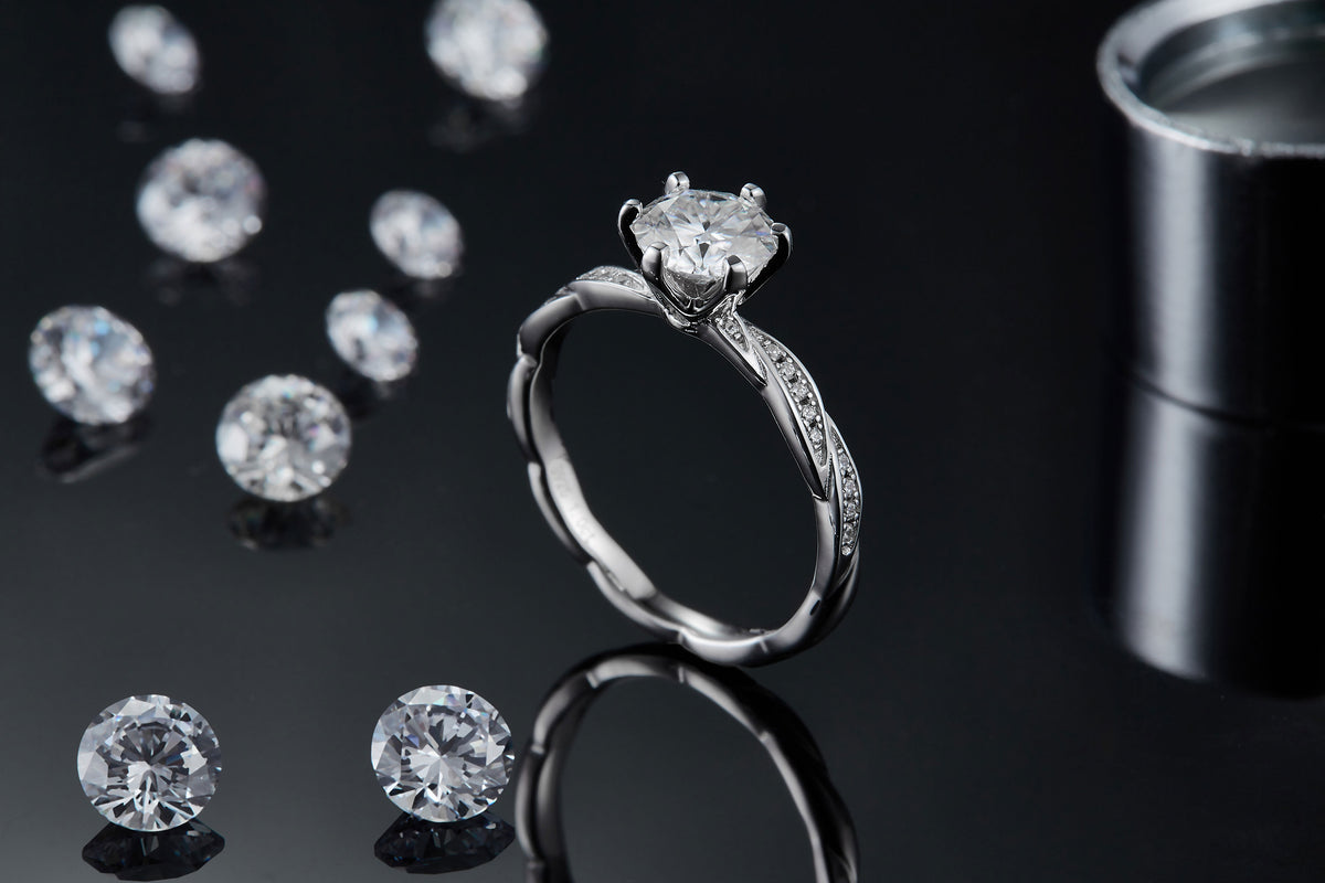 CARISSIE round moissanite solitaire ring, lifestyle shot standing on black surface with loose stones in background