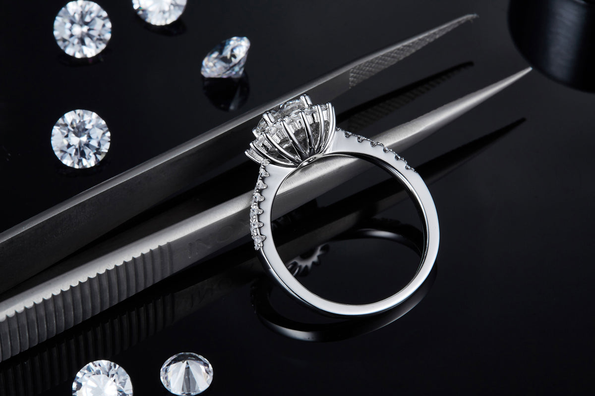 CARISSIE round moissanite halo engagement ring, detailed close-up held by tweezers showing the prong settings and craftsmanship.