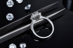 CARISSIE round moissanite halo engagement ring, detailed close-up held by tweezers showing the prong settings and craftsmanship.