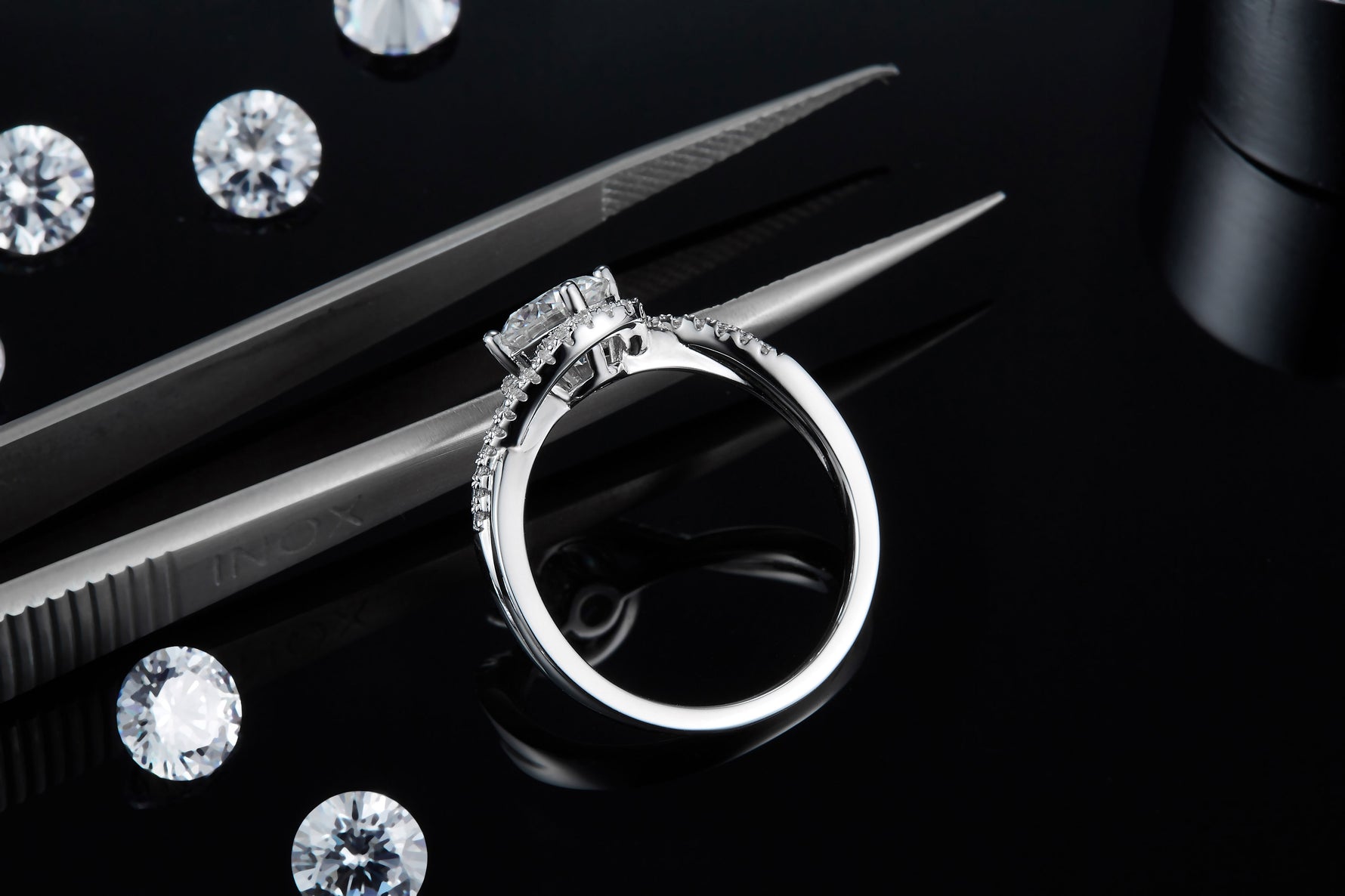 CARISSIE round moissanite solitaire ring, side angle resting near tweezers revealing the gallery structure