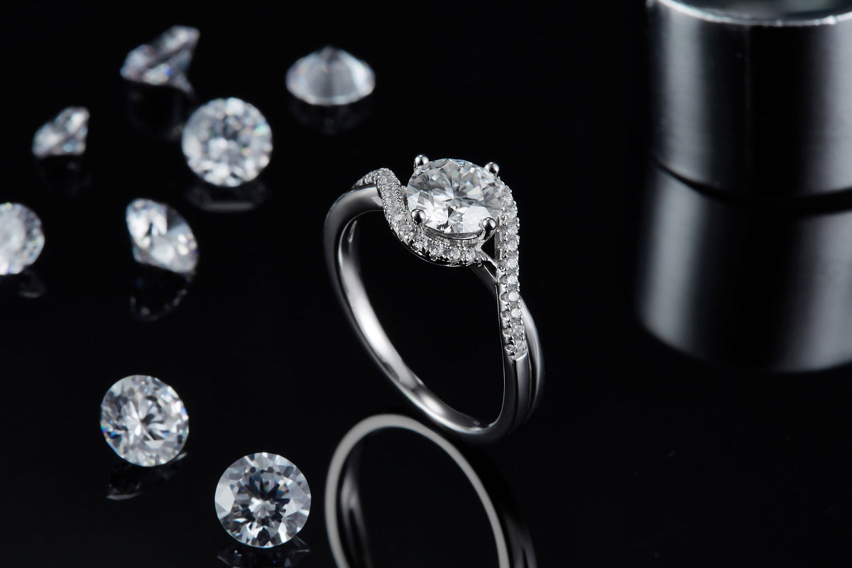 CARISSIE round moissanite solitaire ring, lifestyle shot on black surface surrounded by loose gemstones