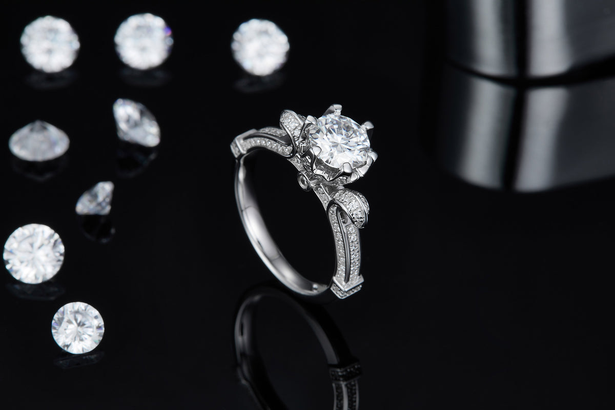 CARISSIE round moissanite solitaire ring, lifestyle shot on black background with loose stones showcasing side sparkle