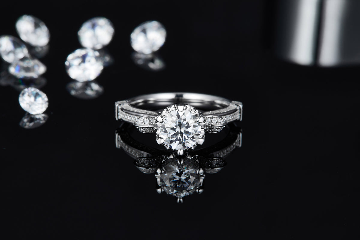 CARISSIE round moissanite solitaire ring, direct front angle on reflective surface emphasizing the stone's fire