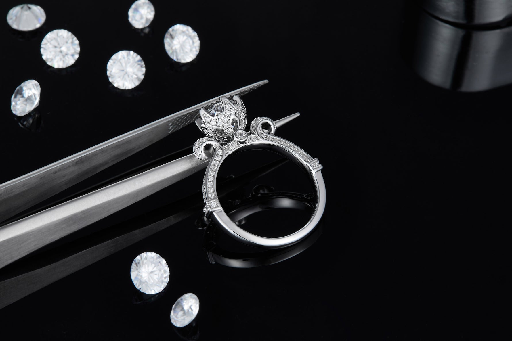 CARISSIE round moissanite solitaire ring, held by tweezers to display the intricate vintage-inspired metalwork details