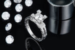 CARISSIE round moissanite solitaire ring, lifestyle shot on black surface displaying sparkle against loose stones and metal cylinder