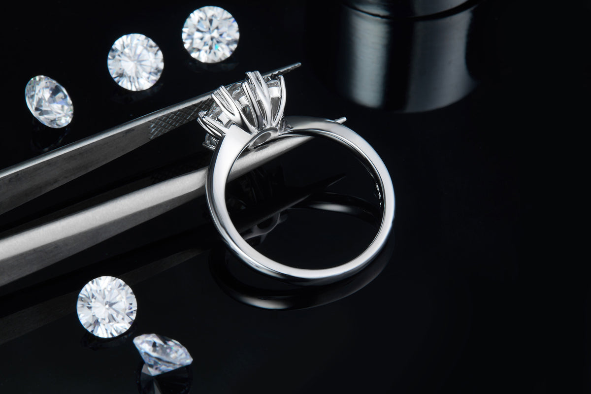 CARISSIE round moissanite cluster ring, held by tweezers to display the interior of the band and gallery work