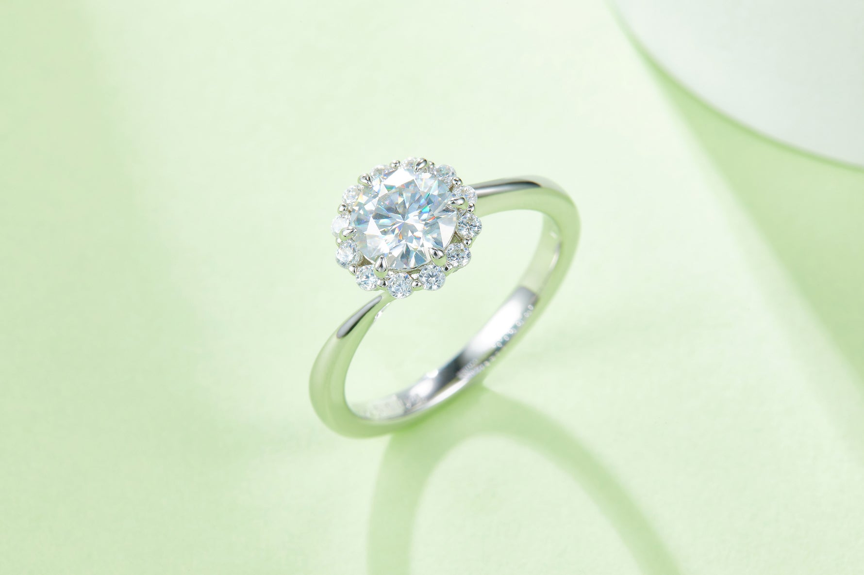 CARISSIE round moissanite halo engagement ring, artistic lifestyle shot on a soft green background highlighting stone sparkle
